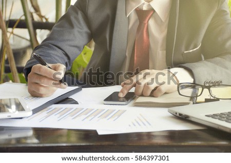 Business man hand holding pen and pointing on smartphone for stock market chart in office.