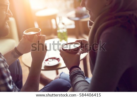 Young couple in love sitting in a cafe, drinking coffee, having a conversation and enjoying the time spent with each other. Selective focus Royalty-Free Stock Photo #584406415