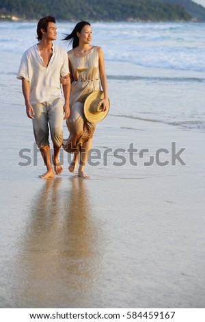 Couple walking on beach, looking away