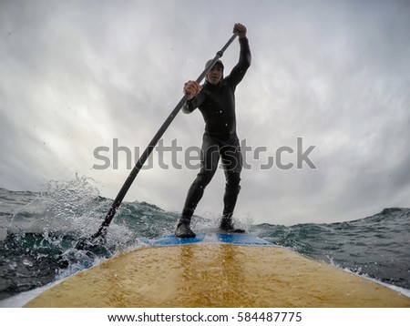 Surfer catching a wave on a paddle board in the ocean. Picture taken in Chesterman Beach, Tofino, Vancouver Island, British Columbia (BC), Canada, during a cloudy winter day.