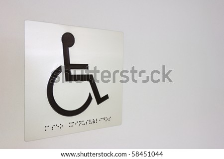 Sign indicating handicapped zone on a white wall and writing Braille