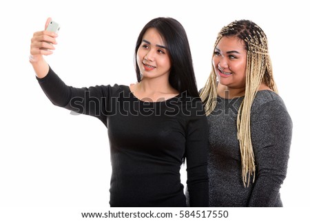 Young happy Asian transgender woman and fat Asian woman smiling while taking selfie picture with mobile phone