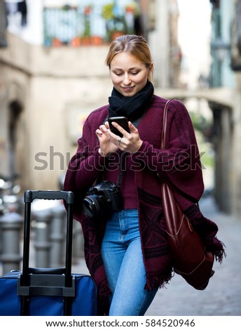 Blond young girl holding phone in hands and looking up her way using app, gps