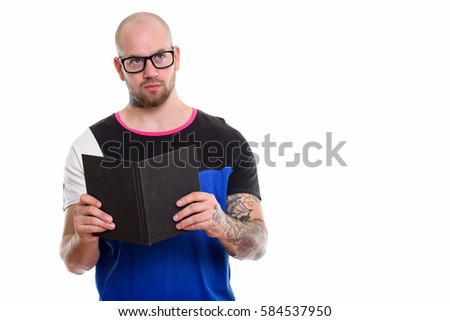 Studio shot of young bald muscular man holding book while thinking and looking up