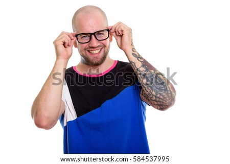 Studio shot of young happy bald muscular man with tattoos smiling while wearing eyeglasses