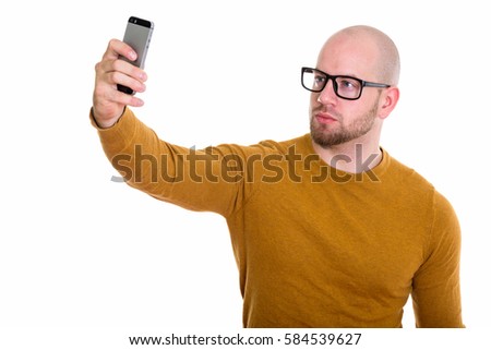 Studio shot of young bald muscular man taking selfie picture with mobile phone