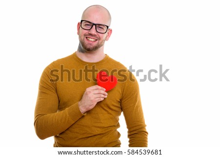 Young happy bald muscular man smiling while holding red heart against chest ready for Valentine's day