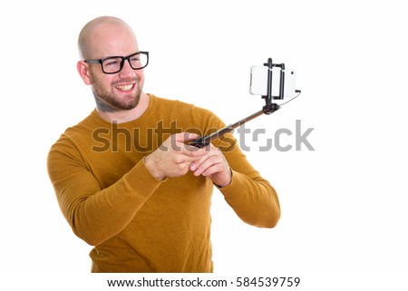 Young happy bald muscular man smiling while holding selfie stick and taking selfie picture with mobile phone