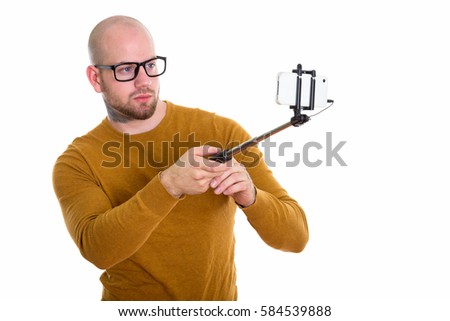 Young bald muscular man holding selfie stick and taking selfie picture with mobile phone