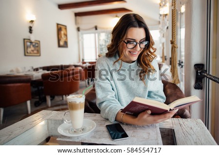 Young  beautiful woman in glasses reading interesting book in cafe   Royalty-Free Stock Photo #584554717