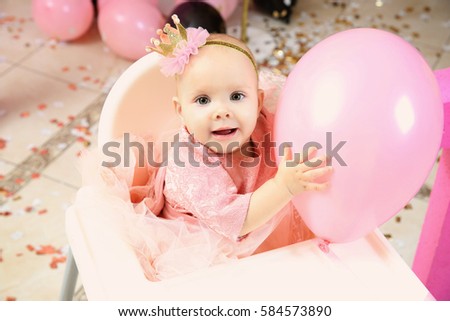 Cute little birthday girl playing with balloon while sitting on high chair