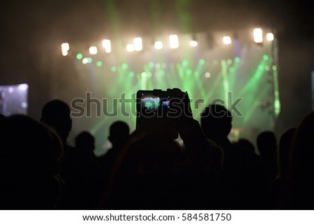 Silhouette of hands using camera phone to take pictures and videos at pop concert, festival.