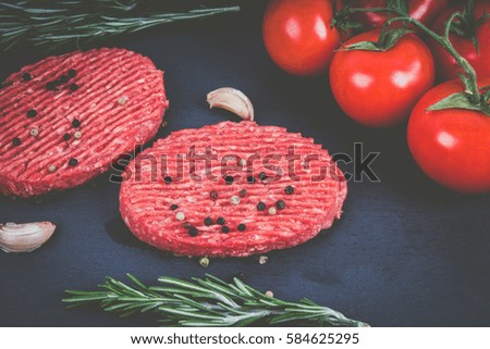 Raw burgers on a slate board with rosemary and garlic. Brown wood background