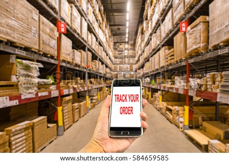 Hand holding smartphone in the warehouse with text track your order.