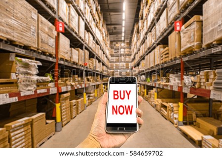 Hand holding smartphone in the warehouse with text buy now
