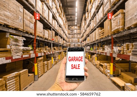 Hand holding smartphone in the warehouse with text garage sale.