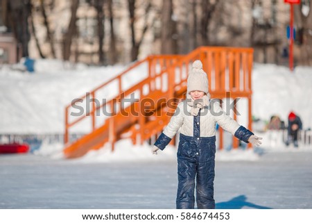 Adorable little girl skating on the ice rink outdoors at warm winter day