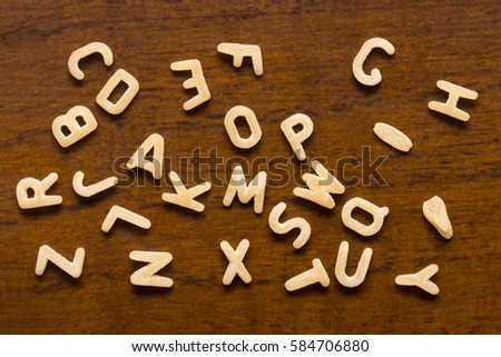 Alphabet made of macaroni letters isolated on wood background.