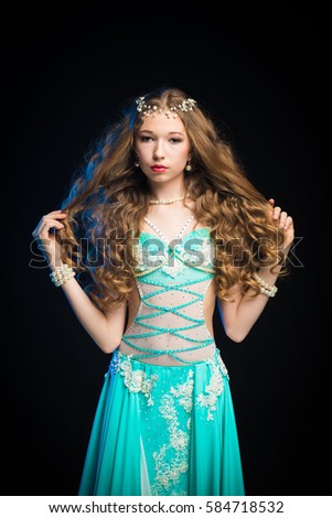 young girl with long hair in a turquoise costume oriental dancer posing and dancing on a black background in the scenic blue light