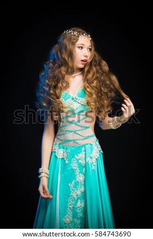 young girl with long hair in a turquoise costume oriental dancer posing and dancing on a black background in the scenic blue light