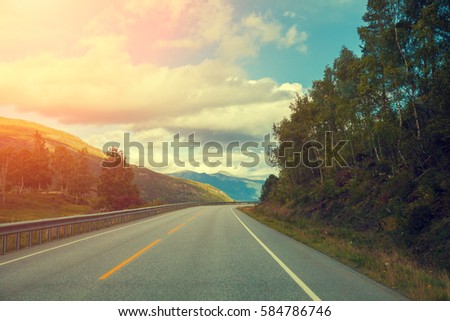 Mountain road at sunset with dramatic cloudy sky.