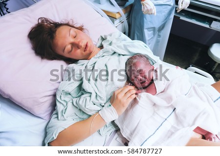 Mother holding her newborn baby child after labor in a hospital. Mother giving birth to a baby boy. Parent and infant first moments of bonding.
