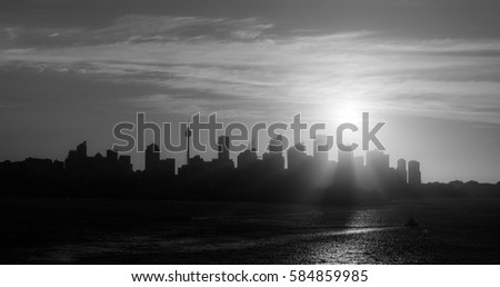 The city of Sydney at sunset with the buildings in silhouette in black and white.