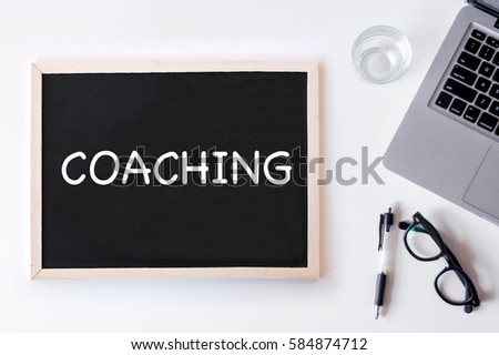 COACHING words written on chalk board with laptop, pen, and glass. Top view with copy space, flat lay.