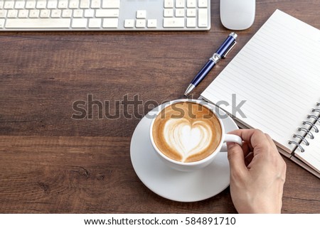 Holding coffee cup of latte art heart shape on wooden table besi