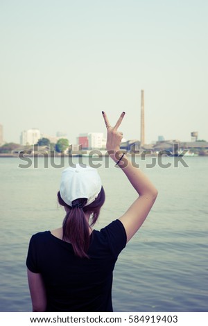 The woman standing on river side and show two finger while looking scenery