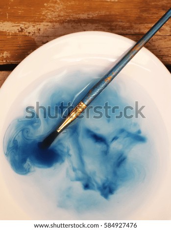 Brush with a blue watercolor paint in a cup of transparent water
