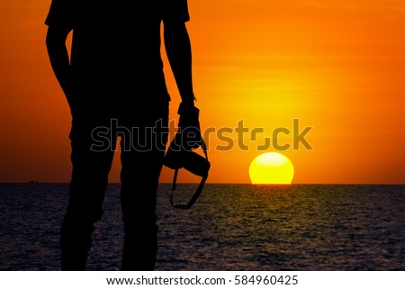Silhouette of young photographer on the beach. Sunset Time