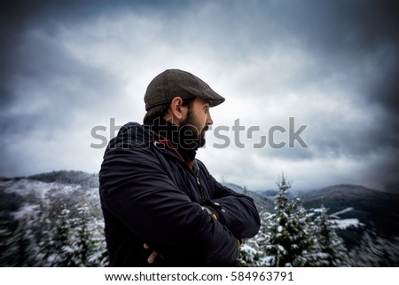 Handsome bearded young man with arms crossed in winter near forest. Outdoor picture.