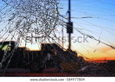 A close view of a shattered glass window pane with cracks extending out of the frame. Blurred buildings can be seen in the background. Royalty-Free Stock Photo #584977804