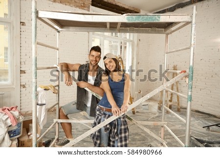 Happy young couple renewing home, smiling under scaffold.