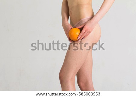 Woman Holding an Orange Against Her Thighs. Healthy skin women without cellulite.