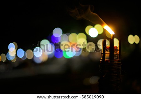 Abstract picture of tropical beach and a flame lighting up at night time. Long exposure shot. Flaming torch at sunset by the pool with colorful bokeh lights on background