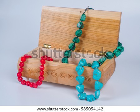 Picture of the opened light-coloured box for bijouterie with turquoise, malachite and coral bead necklaces on white background. Handmade carved jewel box with beads. Side view.