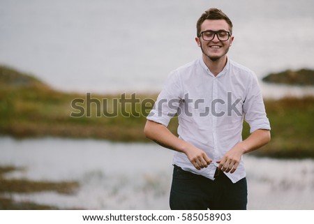 stylish hipster wearing a white shirt and glasses walks by the lake