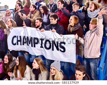 Fans cheering in stadium holding champion banner and singing on tribunes. Large group young people together support your favorite team. Cold weather outdoor.