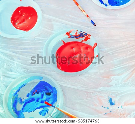 Plates with liquid red and blue paint with brush on the white protective oilcloth. Workplace for children's creativity and drawing. Selective focus.