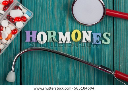 Text "Hormones" of colored wooden letters, stethoscope and pills on a blue wooden background Royalty-Free Stock Photo #585184594