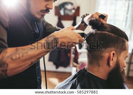 Close up shot of man getting trendy haircut at barber shop. Male hairstylist serving client, making haircut using machine and comb. Royalty-Free Stock Photo #585297881