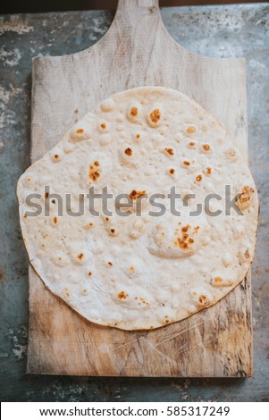 Homemade whole wheat flour tortilla on wooden board, on metal table