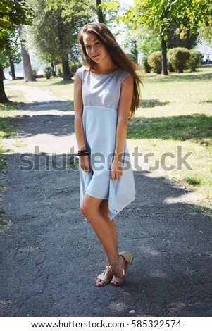 Portrait of beautiful teenage girl in blue blouse, against green of summer park play with her hair.