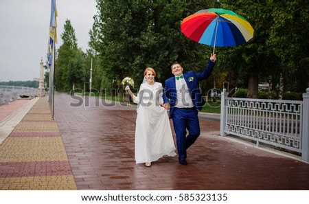 Wedding couple in love under coloured umbrella at rain.