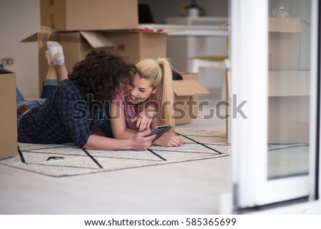 Young couple in love moving in a new flat, lying on the floor and surfing the web on a tablet computer in search of new redecoration ideas