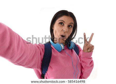 young attractive and happy woman or student girl with backpack and headphones taking selfie photo with mobile phone smiling ecstatic having fun isolated on white background