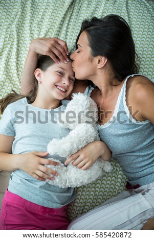 Mother kissing on daughter forehead on bed at home