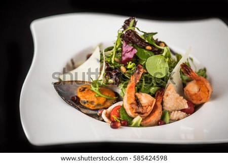 Healthy food. Seafood salad in a white plate on a black background.